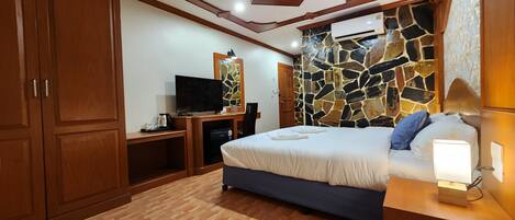A bedroom with a bed, a TV, a desk, and a stone wall.