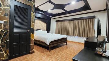 A room with a bed, a desk with a kettle, a TV, and a stone wall.