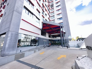 Un edificio moderno con fachada de vidrio, una combinación de colores rojo y blanco, y un letrero que indica apartamentos a la venta.