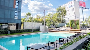 A modern building with a swimming pool, outdoor seating, and greenery. - Apartamento con Alberca y Padel (Mexico City)