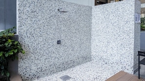 A modern outdoor shower area with mosaic tile walls and floor, a metal showerhead, and a drain cover. - Apartamento con Alberca y Padel (Mexico City)