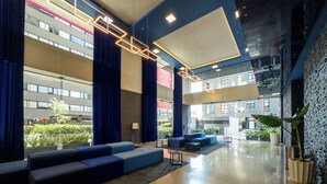 A spacious lobby with a modern design, featuring a seating area with blue sofas and a large open space with a glass wall providing a view of the outside. - Apartamento con Alberca y Padel (Mexico City)