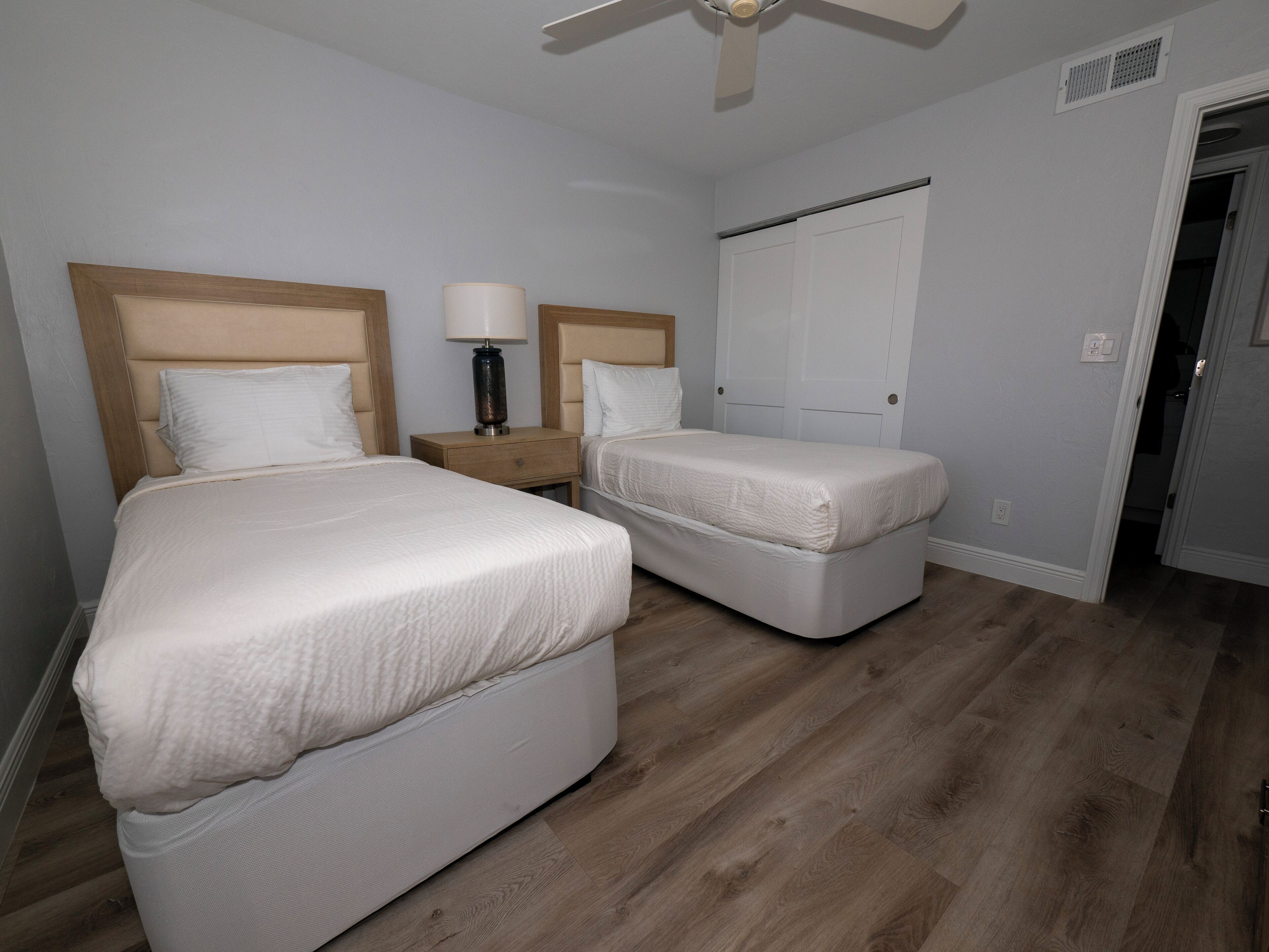Une chambre d’hôtel avec deux lits, une table de chevet avec une lampe, une armoire et un ventilateur de plafond.