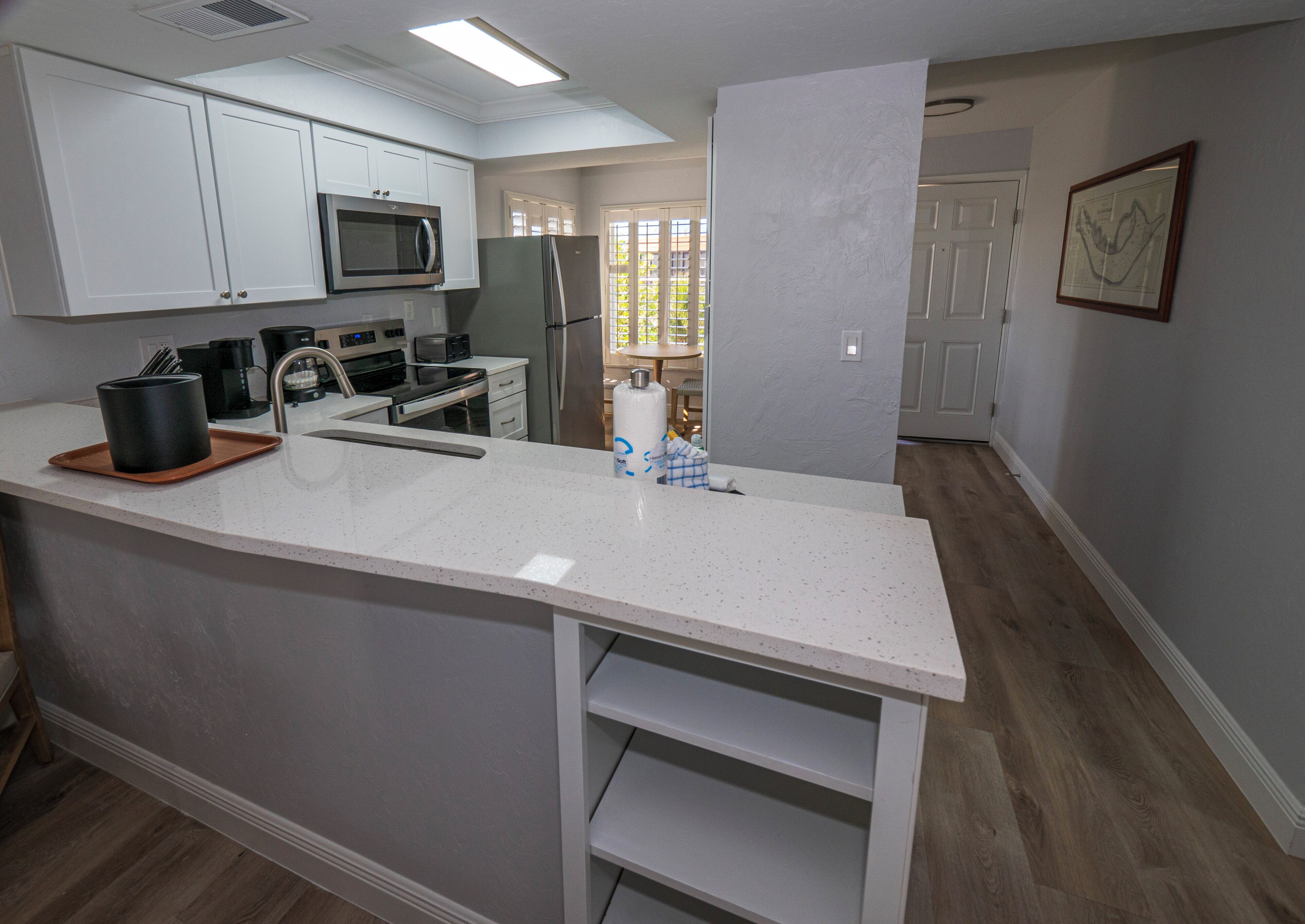 A modern kitchen with white cabinetry, stainless steel appliances, and a white speckled countertop.