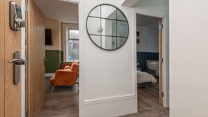 Ein Zimmer mit Holztür, einem runden Spiegel an der Wand, einem Bett und einem Sessel.
