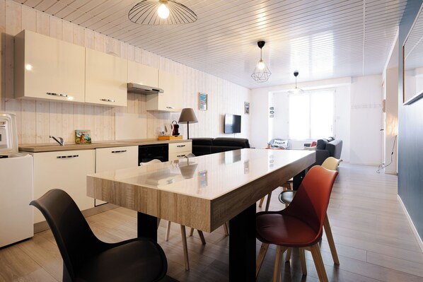 A modern kitchen with a central island, white cabinetry, and a dining area with chairs.