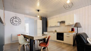 A modern kitchen with wooden cabinets, a dining table with chairs, a clock on the wall, and a ceiling light fixture. - Le reflet des Pyrénées 6/8 people, close to town center and ski shuttles (Bagnères-de-Bigorre)