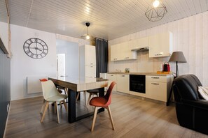 A modern kitchen with wooden cabinets, a dining table with chairs, a clock on the wall, and a ceiling light fixture.