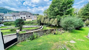 A grassy area with a stone wall and a metal gate, surrounded by trees and a building with multiple windows in the background. - Le reflet des Pyrénées 6/8 people, close to town center and ski shuttles (Bagnères-de-Bigorre)