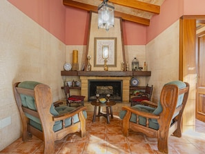 A cozy room with a fireplace, two wooden chairs, a table with glasses, and a decorative mirror on the wall. - Villa Can Emmes · Villa with private pool and ample outdoor space in Alcúdia. (Alcúdia)