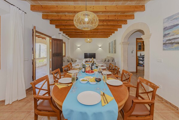Un espace repas avec une longue table dressée pour un repas, des chaises en bois, une nappe bleue et un luminaire suspendu.