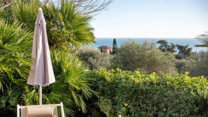 A garden with a view of the sea, a white umbrella, and two beige lounge chairs. - Apartment 'Giardino Miramare' with Sea View, Wi-Fi and Air Conditioning (Imperia)