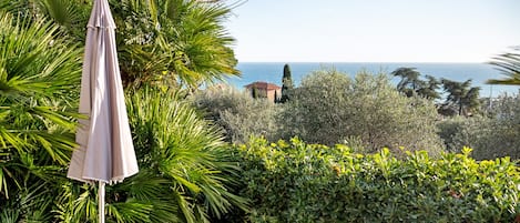 A garden with a view of the sea, a white umbrella, and two beige lounge chairs.