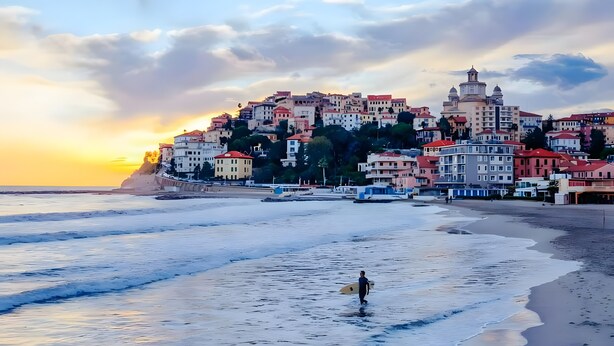 A coastal town with buildings, a beach, and a person with a surfboard. - Apartment 'Giardino Miramare' with Sea View, Wi-Fi and Air Conditioning (Imperia)