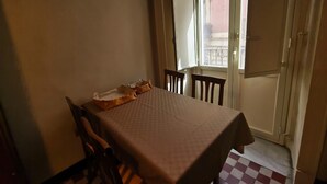 A dining area with a table set for two, a window with a view of buildings, and a door leading outside. - RETROETNEA - Retro-style Apartment in historic center with 2 connecting bedrooms (Catania)
