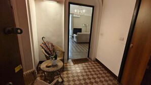 A hallway with a checkered floor, a wicker chair, a small table with a bowl and a potted plant, and a door with a handle. - RETROETNEA - Retro-style Apartment in historic center with 2 connecting bedrooms (Catania)