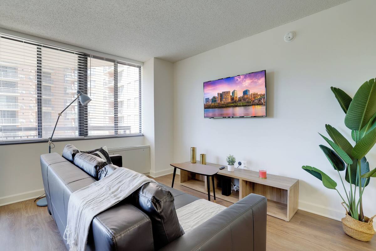 A modern living room with a grey sofa, a wooden coffee table, a large potted plant, and a cityscape painting on the wall.