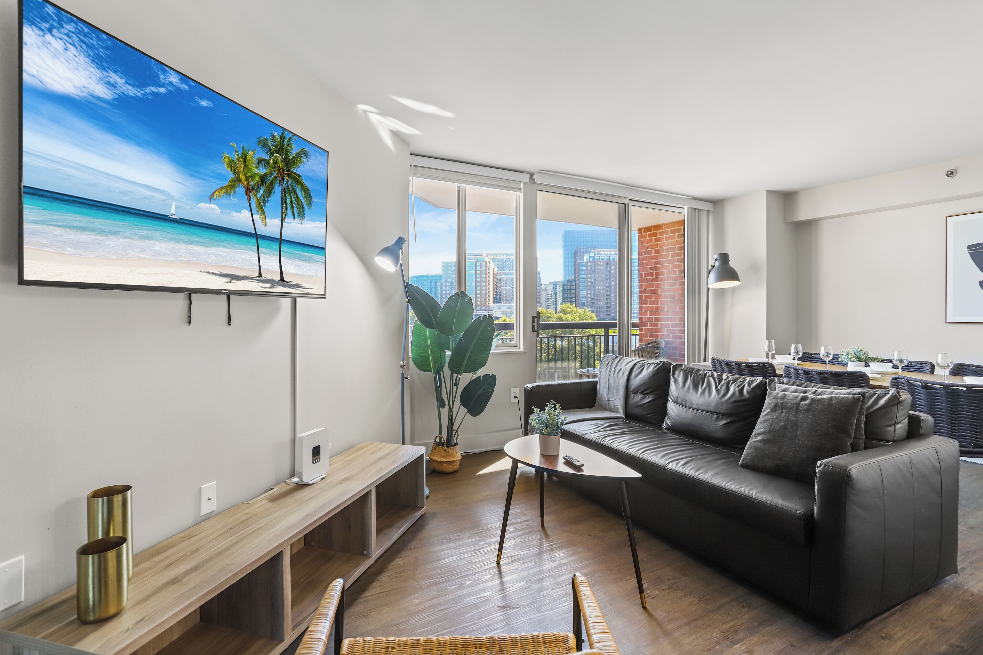 Ein modernes Wohnzimmer mit großem Fernseher, einer Ledersofa, einem Couchtisch und Blick auf die Stadt durch große Fenster.