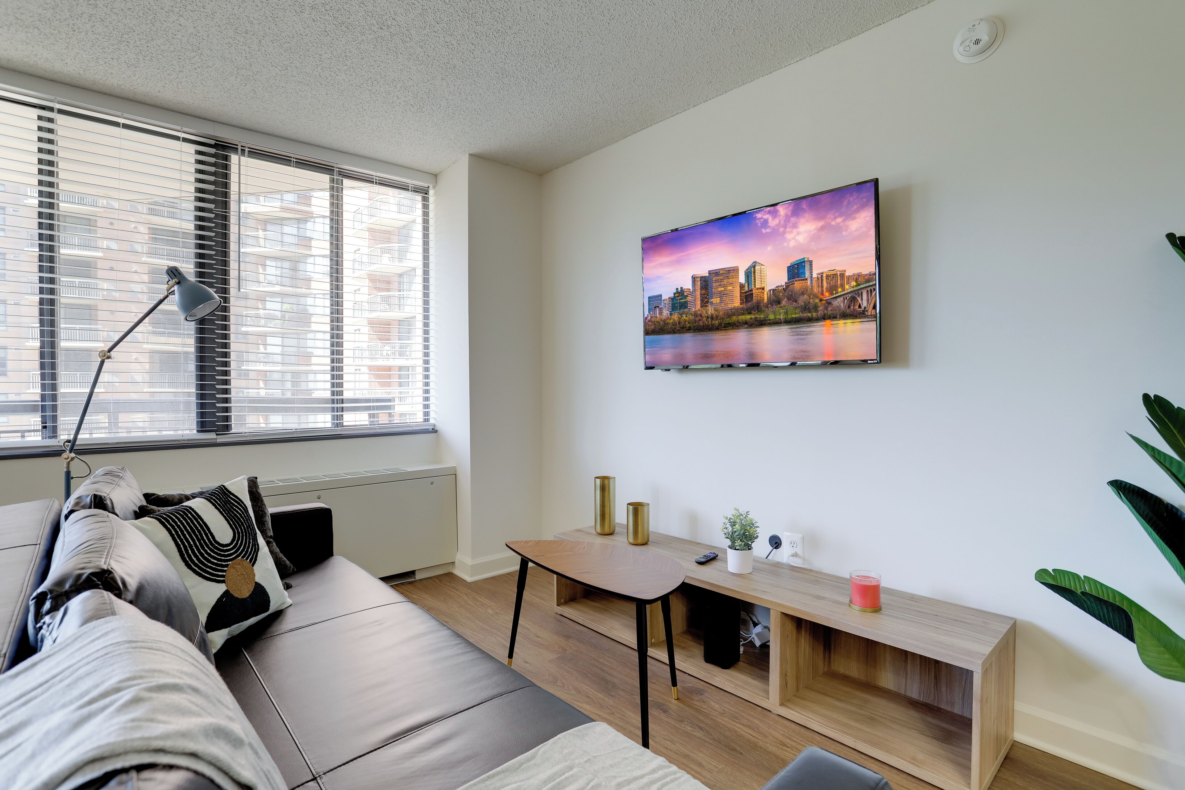 Een moderne woonkamer met een bank, een tafel, een lamp en een stadsgezichtschilderij aan de muur.