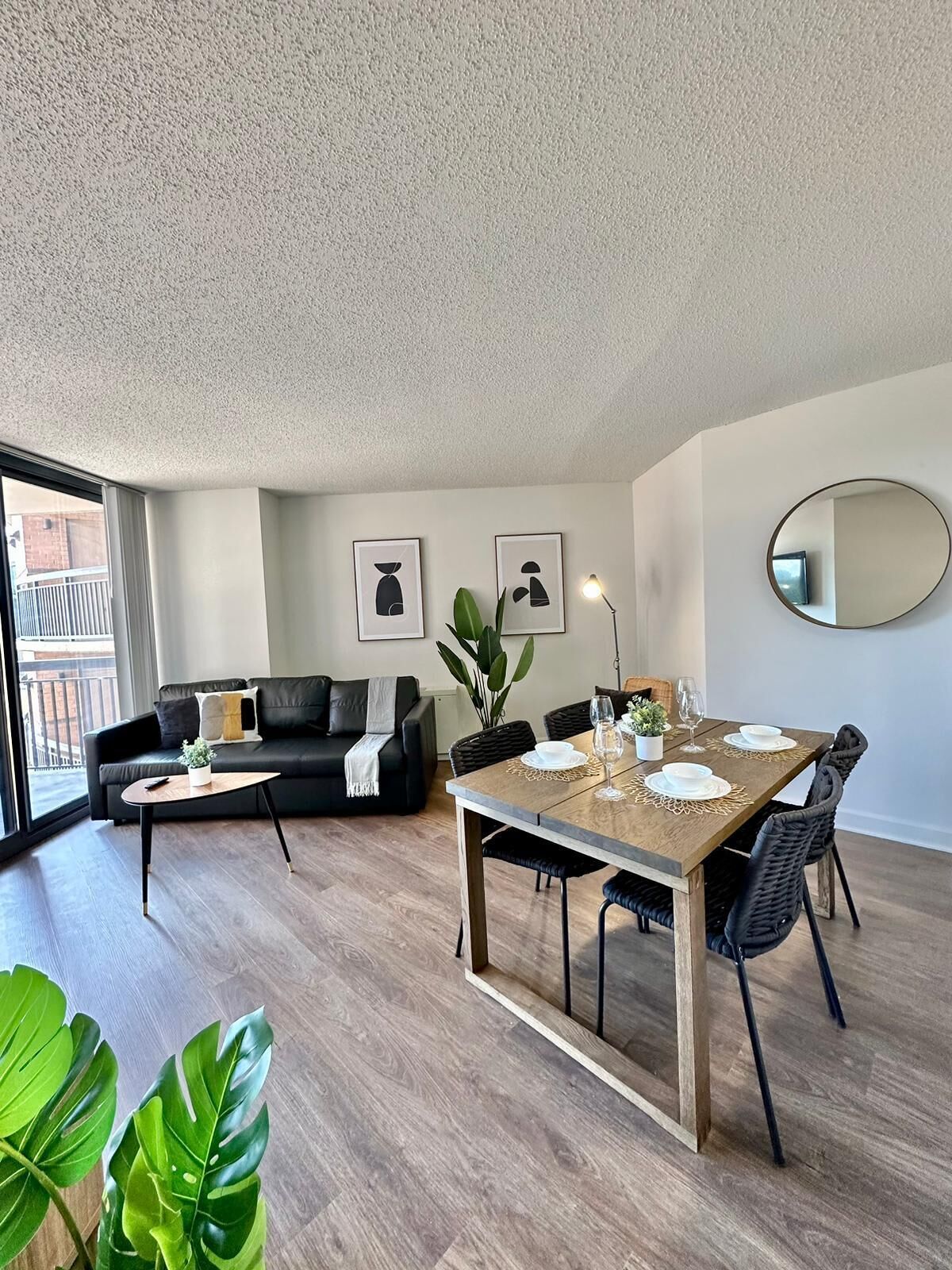Ein modernes Wohnzimmer mit Essbereich, ausgestattet mit einer Couch, einem Couchtisch, einem Esstisch für vier Personen und einem großen Fenster mit Blick nach draußen.