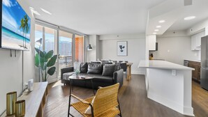 Un salon moderne avec un canapé noir, un coin repas et une cuisine.