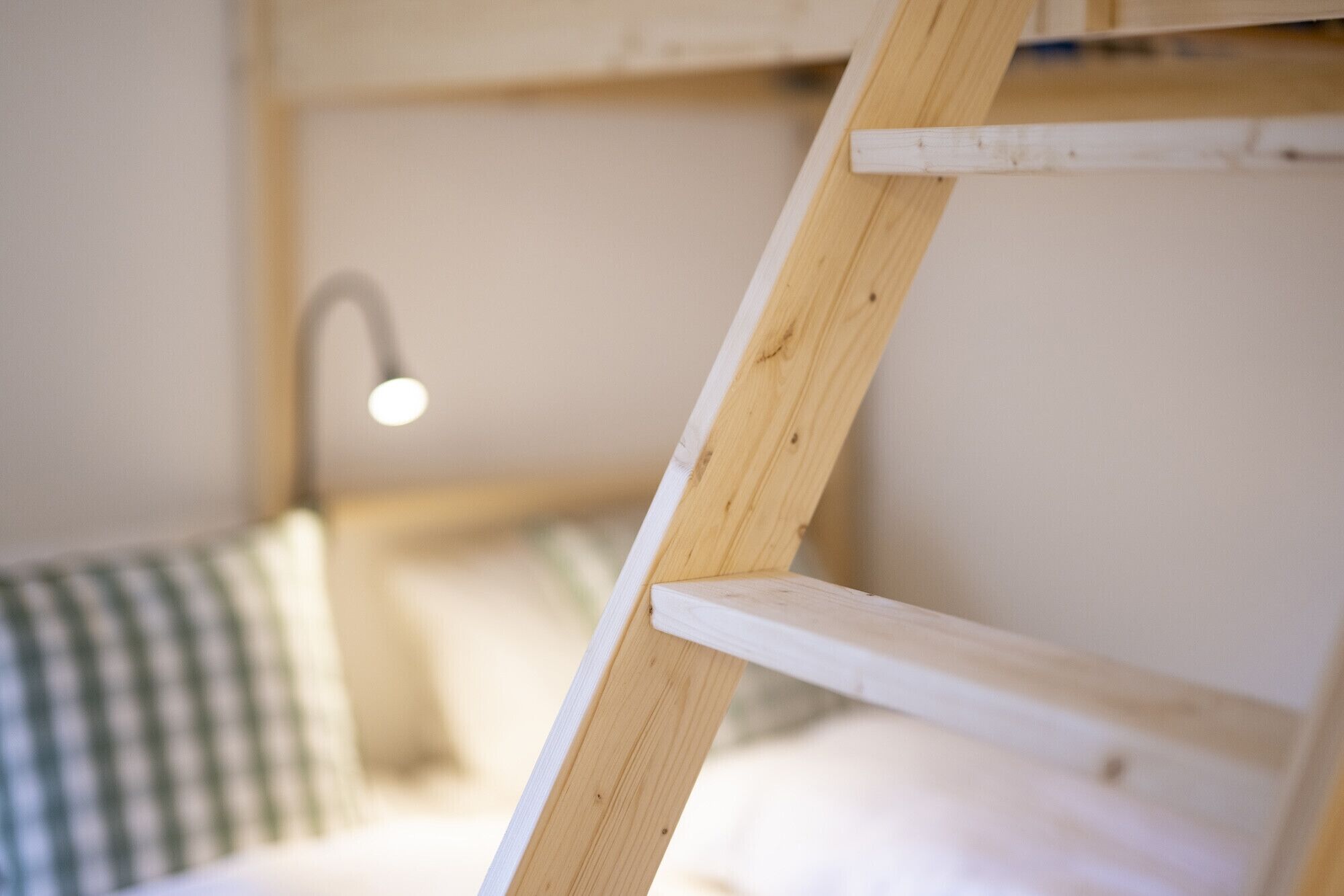 Une échelle en bois appuyée contre un lit superposé doté d’une tête de lit blanche.