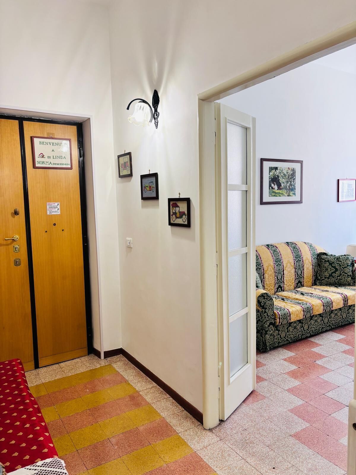 Ein Hotelzimmer mit einer Holztür, einem roten und gelben Streifen Teppich, einer gepolsterten Couch mit Muster und gerahmten Bildern an der Wand.