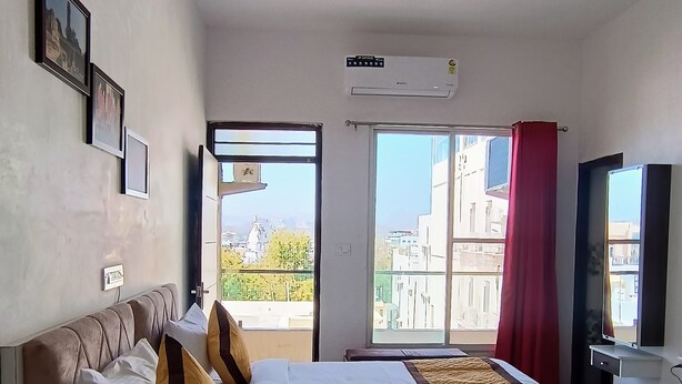 Habitación de hotel con cama, televisor, ventana con vistas a edificios y equipo de aire acondicionado.