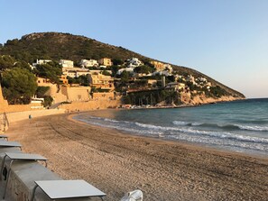 A coastal beach with buildings on a hillside, sandy beach, and calm sea.