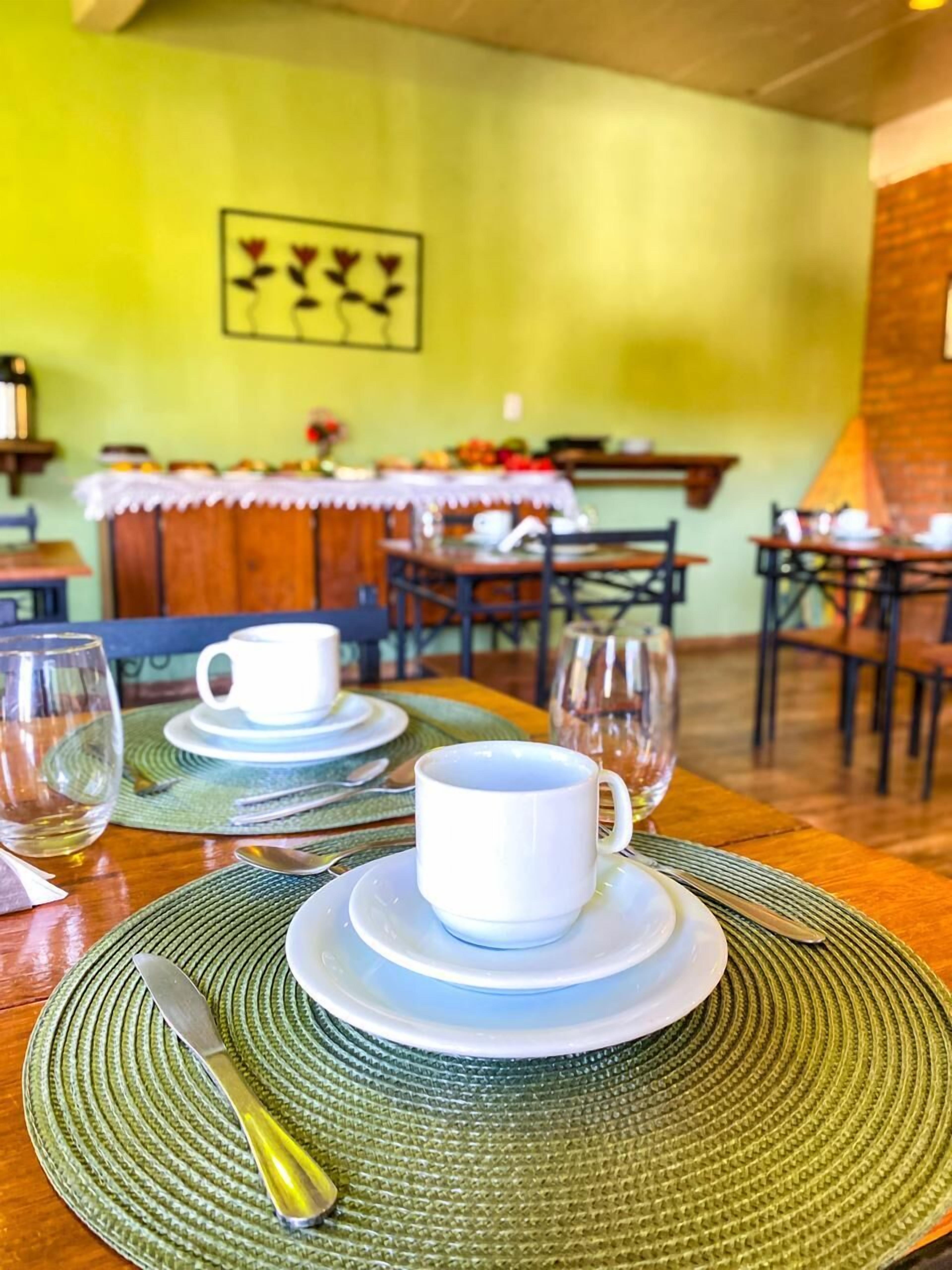 A dining table set with white cups and saucers, a clear glass, and a metal spoon on a green placemat.