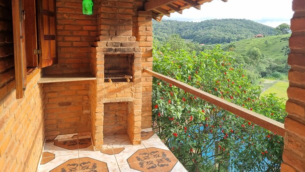 Una chimenea de ladrillo rústica con un estante de madera y un farol verde colgante, con vistas a un exuberante valle verde.