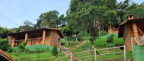 A rural house with a green roof, surrounded by lush greenery and a hillside.