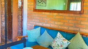 Un cuarto acogedor con una mesa de madera dispuesta para dos personas, un sofá verde con cojines, un espejo con un marco ornamentado y una pared de ladrillo.