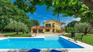 A pool with lounge chairs, a yellow house with a balcony, and trees in the background. - Picturesque flat with pool, outdoor kitchen, BBQ, sunbeds, children's swing (Sv. Lovrec)