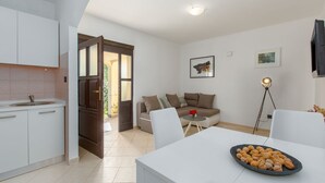 A modern kitchen with white cabinets, a dining area with a white table and chairs, a sofa, and a floor lamp. - Picturesque flat with pool, outdoor kitchen, BBQ, sunbeds, children's swing (Sv. Lovrec)