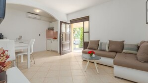 A modern living room with a sofa, a dining table, and a kitchen area visible through an open door. - Picturesque flat with pool, outdoor kitchen, BBQ, sunbeds, children's swing (Sv. Lovrec)