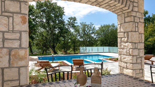Una pérgola de piedra con vistas a una piscina y zona de estar al aire libre.