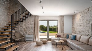 Ein modernes Wohnzimmer mit Steinwand, Holztreppe, einer Sofagarnitur und Blick auf einen Swimmingpool.