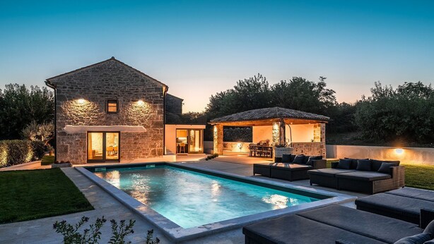 Ein modernes Haus mit Swimmingpool, Sitzgelegenheit im Freien und einer Stein-Fassade.