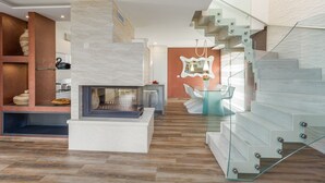 A modern interior with a fireplace, a glass staircase, and a dining area with a glass table and chairs.