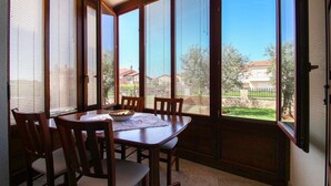 A dining area with a table and chairs, large windows with blinds, and a view of a residential neighborhood. - Picturesque flat with pool, private terrace, washing machine, BBQ, loungers (Novigrad)