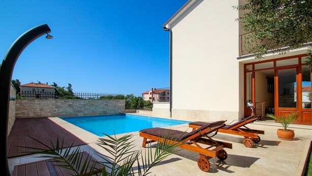 A swimming pool with lounge chairs, a stone wall, and a building with a balcony. - Picturesque flat with pool, private terrace, washing machine, BBQ, loungers (Novigrad)