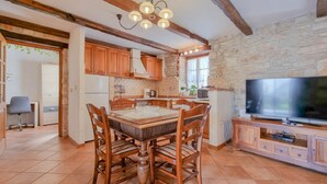 Eine gemütliche Küche mit Holzschränken, einem Esstisch mit Stühlen, einem Fernseher auf einem Holzboden und einer Steinwand.
