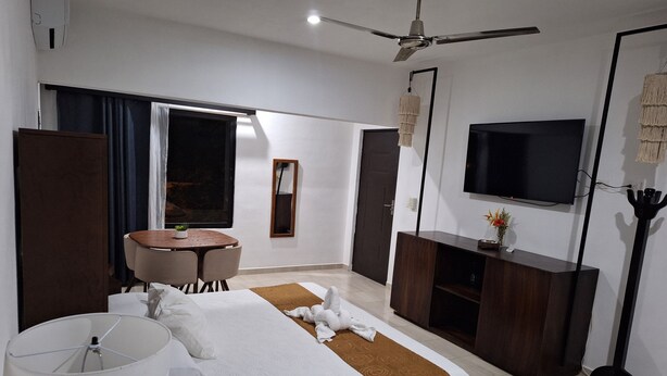 A modern hotel room with a bed, a desk, a chair, a TV, and a ceiling fan. - Casa Yaxche (Valladolid)