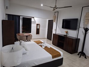 Ein modernes Hotelzimmer mit einem Bett, einem Schreibtisch, einem Sessel, einem Fernseher und einem Deckenventilator.