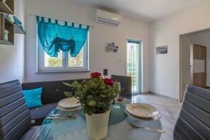 A dining area with a glass table, a sofa, and a window with blue curtains. - Dog-friendly flat with BBQ, private balcony and only 700 metres to the beach (Crikvenica)