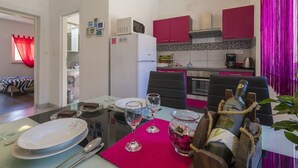 A modern kitchen with red cabinets, a microwave, and a stove. There is a dining area with a table set for two, including plates, glasses, and a bottle of wine. - Charming dog-friendly flat with private balcony, playground, barbecue (Crikvenica)