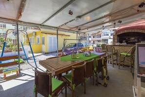 An outdoor patio with a table and chairs, a brick oven, and a playground in the background. - Charming dog-friendly flat with private balcony, playground, barbecue (Crikvenica)