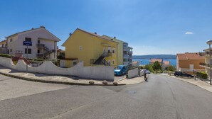 A street with a yellow building, a staircase, and a blue car parked on the side. - Charming dog-friendly flat with private balcony, playground, barbecue (Crikvenica)