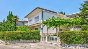 A two-story house with a stone facade, a balcony with a white railing, and a gated entrance. - Cosy flat just 200 metres from the sandy beach with sea views, barbecue, air conditioning (Crikvenica)